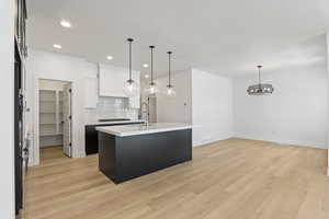 Kitchen featuring tasteful backsplash, light countertops, white cabinets, recessed lighting, and an island with sink