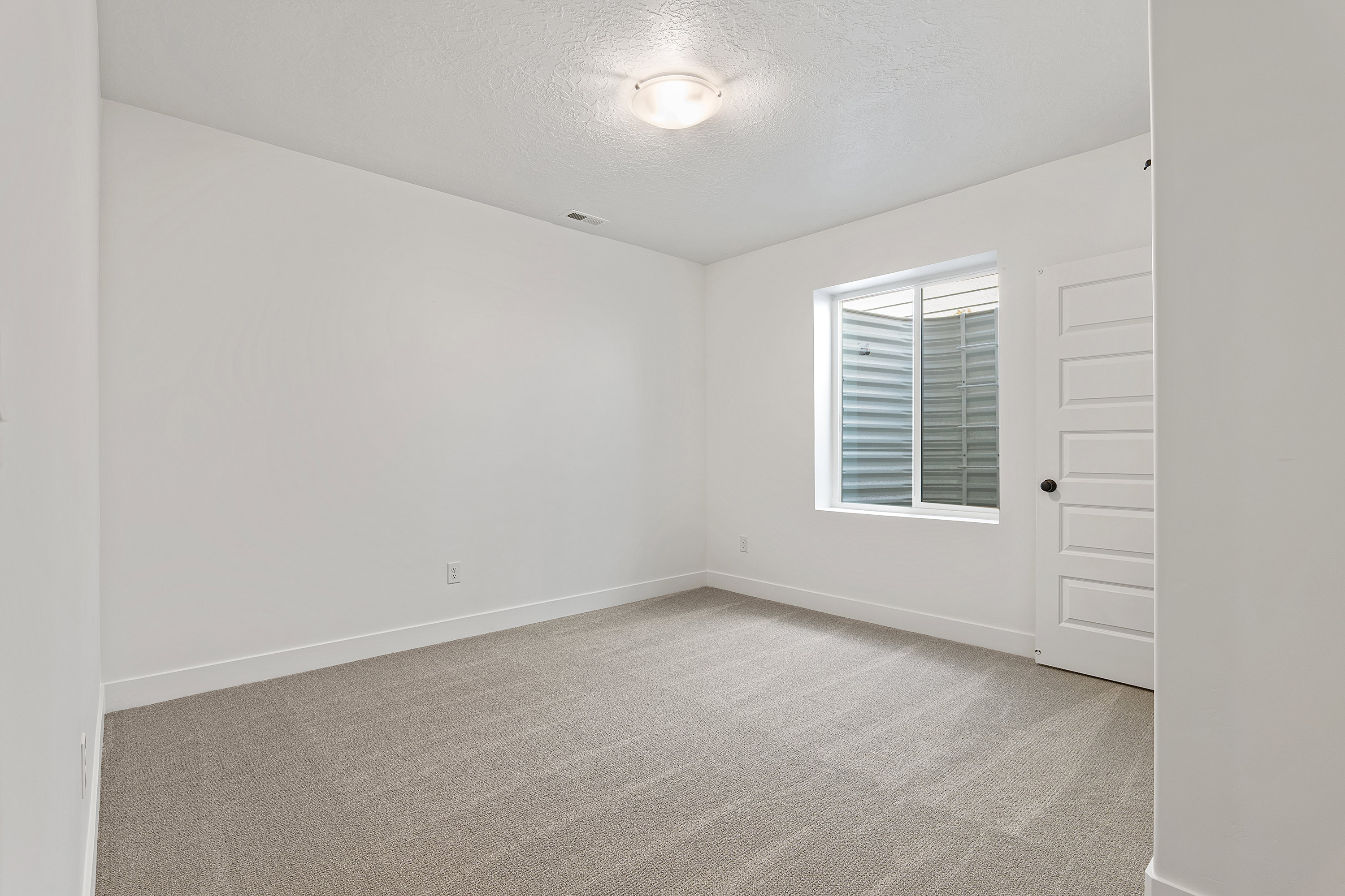 Empty room with light colored carpet and a textured ceiling
