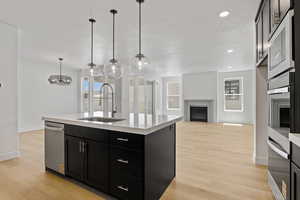 Kitchen with a fireplace, dark cabinetry, light countertops, light wood finished floors, and appliances with stainless steel finishes