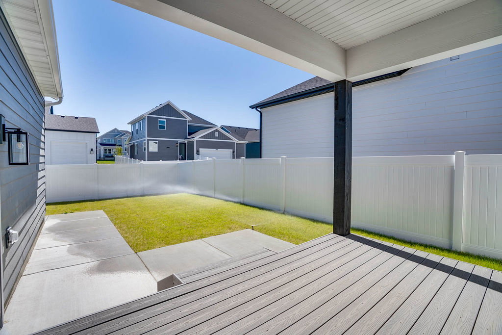 Covered deck with composite decking, featuring a white vinyl privacy fence, a manicured lawn, and concrete patio areas