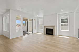 Unfurnished living room featuring light wood-style floors, a fireplace, a textured ceiling, and recessed lighting