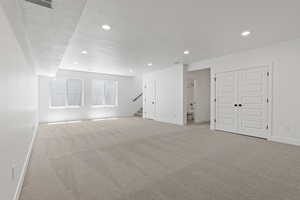 Basement featuring light colored carpet, a textured ceiling, recessed lighting, and stairway