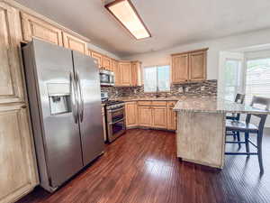 Kitchen featuring a peninsula, appliances with stainless steel finishes, light brown cabinets, a kitchen breakfast bar, and a textured ceiling