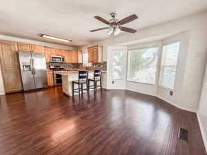 Kitchen featuring stainless steel appliances, dark wood-type flooring, a ceiling fan, backsplash, and a kitchen breakfast bar