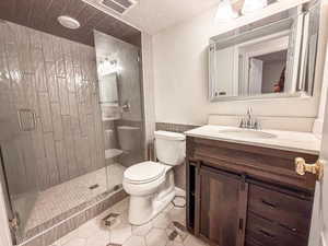 Full bath featuring a textured ceiling, vanity, a shower stall, and tile patterned flooring