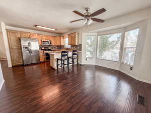 Kitchen featuring appliances with stainless steel finishes, dark wood-style floors, a ceiling fan, a peninsula, and backsplash