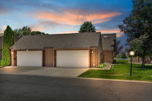 View of front facade featuring brick siding, a front lawn, roof with shingles, and driveway