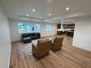 Living room with a raised ceiling, recessed lighting, and light wood-style floors