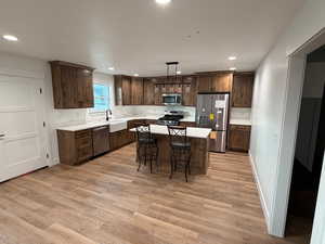 Kitchen with appliances with stainless steel finishes, light wood finished floors, decorative light fixtures, recessed lighting, and dark brown cabinets