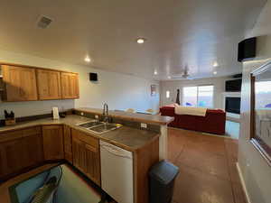 Kitchen with a peninsula, white dishwasher, a fireplace, dark tile patterned flooring, and dark countertops.  Some furnishings have changed.