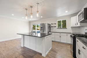 Kitchen featuring stainless steel appliances, tasteful backsplash, white cabinetry, dark wood finished floors, and a center island with sink