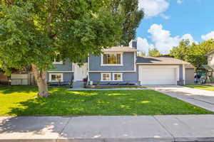 Raised ranch with driveway, an attached garage, a front lawn, a chimney, and stucco siding