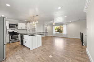 Kitchen with crown molding, stainless steel appliances, open shelves, recessed lighting, and open floor plan