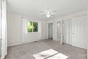 Unfurnished bedroom with carpet flooring, two closets, and ceiling fan