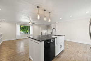 Kitchen featuring dishwasher, open floor plan, light wood-type flooring, a center island with sink, and ornamental molding