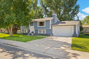 Raised ranch featuring a garage, a front yard, concrete driveway, a chimney, and stone siding