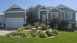 View of front facade featuring stone siding, a front yard, concrete driveway, and an attached garage