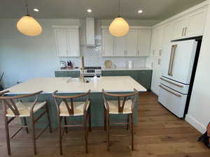 Kitchen with high end white refrigerator, dark wood-type flooring, wall chimney exhaust hood, backsplash, and light countertops