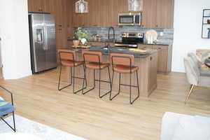 Kitchen featuring stainless steel appliances, decorative backsplash, brown cabinetry, and a kitchen bar