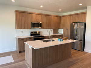 Kitchen featuring stainless steel appliances, recessed lighting, light countertops, brown cabinetry, and light wood-type flooring