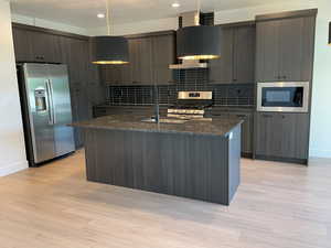Kitchen with appliances with stainless steel finishes, modern cabinets, a textured ceiling, a center island with sink, and dark stone countertops