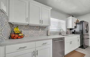 Kitchen with stainless steel appliances, tasteful backsplash, white cabinets, light countertops, and light tile patterned floors