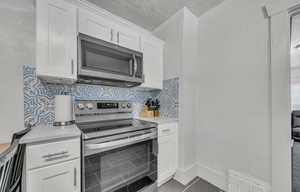 Kitchen with appliances with stainless steel finishes, light countertops, white cabinetry, a textured ceiling, and tile patterned floors