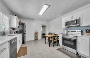 Kitchen with stainless steel appliances, a textured ceiling, decorative backsplash, light countertops, and white cabinets