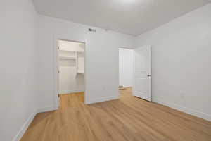 Unfurnished bedroom featuring light wood-type flooring, a walk in closet, and a textured ceiling