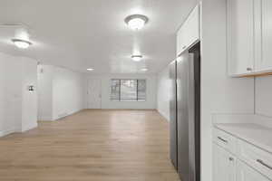 Interior space featuring white cabinetry, a textured ceiling, light wood finished floors, freestanding refrigerator, and open floor plan