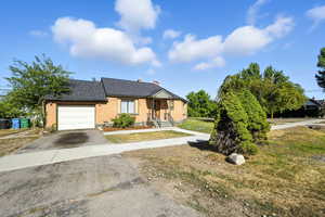View of front of house featuring an attached garage, a shingled roof,  driveway, brick siding, and a chimney.