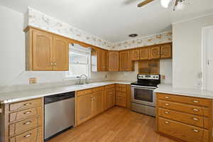 Kitchen featuring appliances with stainless steel finishes, laminate flooring, wood cabinetry, and light countertops.