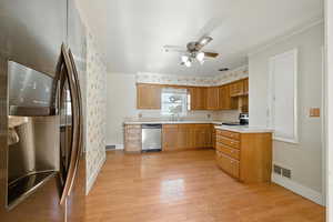Kitchen featuring appliances with stainless steel finishes, light countertops, light laminate flooring, ceiling fan, and wood cabinets.
