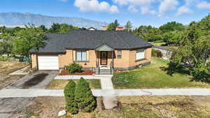 View of front featuring a chimney, roof with shingles, brick siding, and driveway.