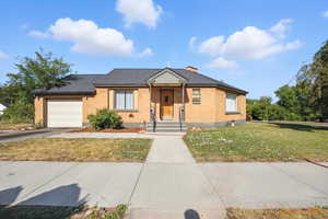 View of front facade with a garage, roof with shingles, brick siding, a front yard, and driveway.