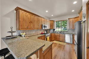 Kitchen with a peninsula, tasteful backsplash, light wood-style flooring, stainless steel appliances, and recessed lighting