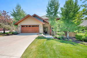 View of front of house featuring stone siding, an attached garage, a front yard, concrete driveway, and stucco siding