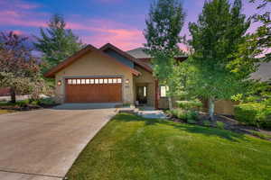 View of front facade featuring stone siding, a front yard, an attached garage, stucco siding, and concrete driveway