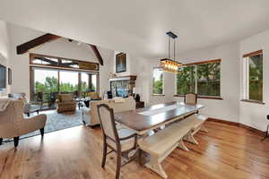 Dining area with a fireplace, plenty of natural light, light wood finished floors, beam ceiling, and high vaulted ceiling