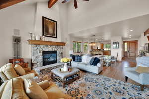 Living room featuring light wood-type flooring, a fireplace, ceiling fan, high vaulted ceiling, and beam ceiling
