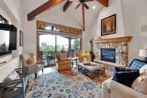 Living area featuring beamed ceiling, high vaulted ceiling, a stone fireplace, a ceiling fan, and recessed lighting