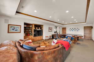 Carpeted living area with a raised ceiling, recessed lighting, and crown molding