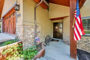 Property entrance with stone siding, covered porch, and stucco siding