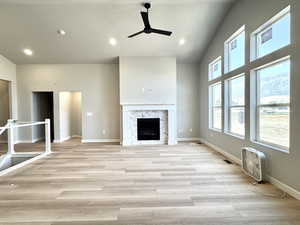 Unfurnished living room featuring light wood-type flooring, a ceiling fan, a fireplace, recessed lighting, and high vaulted ceiling