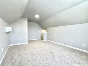 Bonus room with vaulted ceiling, a textured ceiling, and carpet flooring