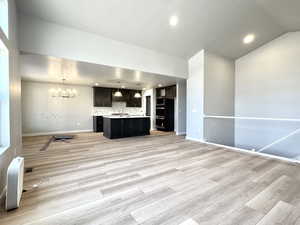Unfurnished living room with light wood-style floors, recessed lighting, a chandelier, and lofted ceiling