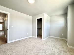 Unfurnished bedroom featuring light carpet, a textured ceiling, and a walk in closet