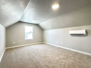Additional living space with carpet, a textured ceiling, lofted ceiling, and a wall mounted AC