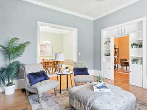 Living area with crown molding, light wood-style flooring, built in features, and a chandelier