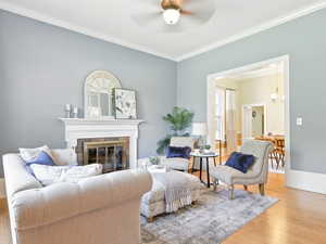 Living room featuring light wood finished floors, ornamental molding, a glass covered fireplace, and a ceiling fan